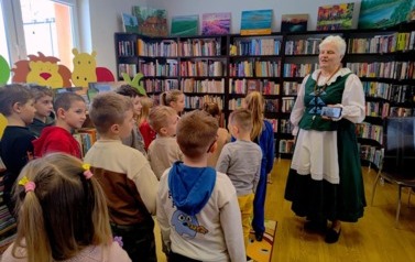 Pani Krysia stoi przy dzieciach i pokazuje na telefonie nagranie hymnu kociewskiego i razem z dziećmi śpiewa