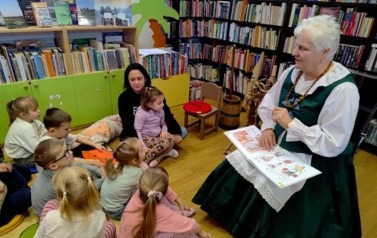 Dzieci siedzą na dywanie i patrzą na Panią Krysię, kt&oacute;ra im czyta ciekawostki kociewskie