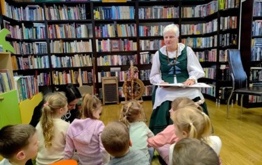 Dzieci siedzą na dywanie i patrzą na Panią Krysię, kt&oacute;ra im czyta ciekawostki kociewskie