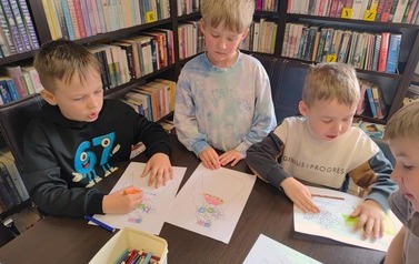 Trzech chłopc&oacute;w przy stole kolorują Panią Wiosnę.