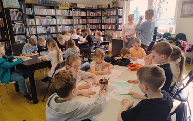 Duża grupa dzieci przy trzech stołach wykonuje wiosenne prace plastyczne, obok stoją ich Panie.