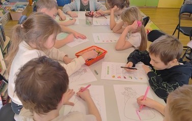 Dzieci przy długim białym stole wykonują wiosenne prace plastyczne