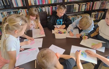 Dzieci przy stole wykonują prace plastyczne. Kolorują Pania Wiosnę i rysują wiosenne szlaczki.