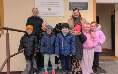 Dzieci wraz z dwiema Paniami z Przedszkola stoją przed budynkiem biblioteki w Pinczynie.