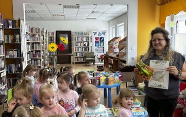 Dzieci stoją w grupie obok bibliotekarki, kt&oacute;ra trzyma podziękowanie i toffifi owinięte zieloną wstążeczką