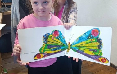 Bibliotekarka z dziewczynką trzymają otwartą książkę w kt&oacute;rej jest pokazany piękny motyl