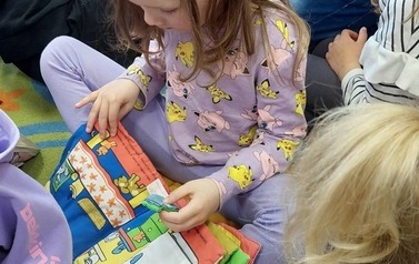 Dzieci siedzą na siedziskach i bawią się pluszowymi książeczkami.