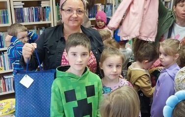 Dzieci ubierają się szykując do wyjścia, przy nich stoi bibliotekarka trzymając granatową torbę papierową.