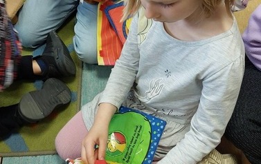 Dwie dziewczynki bawią się pluszowymi książeczkami, obok widać inne dzieci.