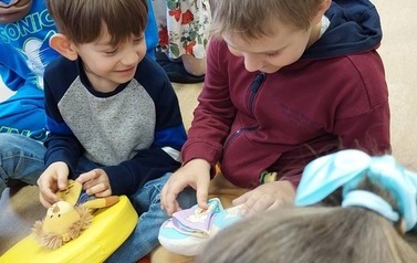 Dzieci siedzą na siedziskach i bawią się pluszowymi książeczkami.
