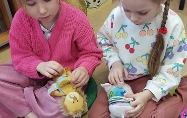 Dwie dziewczynki siedzą na siedziskach i bawią sie pluszowymi książeczkami.