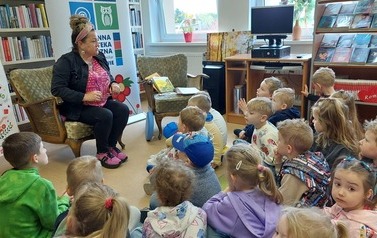 Dzieci siedzą na siedziskach i patrzą na bibliotekarkę, kt&oacute;ra do nich m&oacute;wi.
