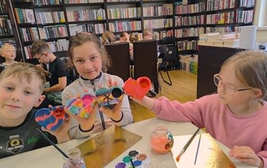 Dwie dziewczynki i chłopiec siedzą przy stole i pokazują swoje pomalowane serca.