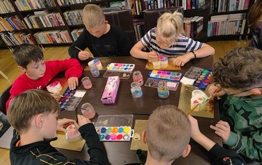 Dzieci siedzą przy stole i malują farbkami serduszka z gipsu