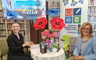 Pisarka przy stoliku podpisuje na książce dedykację czytelniczce, kt&oacute;ra siedzi obok. Obie się uśmiechają.
