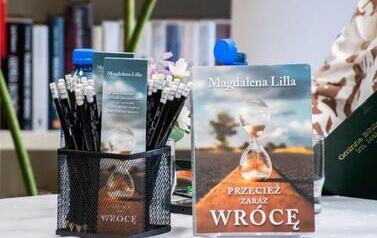 Na okrągłym stoliku stoi książka pisarki pt 'Przecież zaraz wr&oacute;cę" i w pudełku są oł&oacute;wki i zakładki do książki z logiem pisarki.