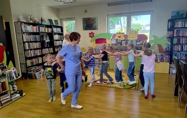 Dzieci robią pociąg, ustawieni jedno za drugim za Panią Gabrysią, kt&oacute;ra prowadzi ten pociąg do muzyki "Lokomotywa"