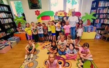 Pani Jolanta Gdaniec stoi z całą grupa dzieci, część dzieci siedzi na dywanie