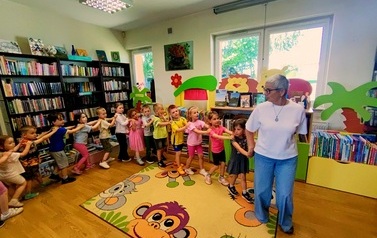 Dzieci robią pociąg, ustawieni jedno za drugim za Panią Jolą, kt&oacute;ra prowadzi ten pociąg do muzyki "Lokomotywa"