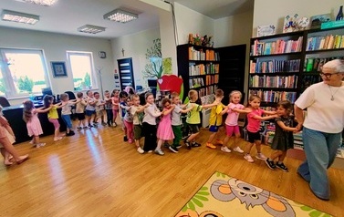 Dzieci robią pociąg, ustawieni jedno za drugim za Panią Jolą, kt&oacute;ra prowadzi ten pociąg do muzyki "Lokomotywa"