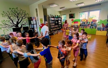 Dzieci robią pociąg, ustawieni jedno za drugim za Panią Jolą, kt&oacute;ra prowadzi ten pociąg do muzyki "Lokomotywa"