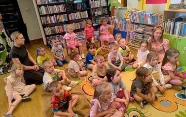 Dzieci siedzą wraz ze swoją nauczycielką na dywanie i słuchają bajki.