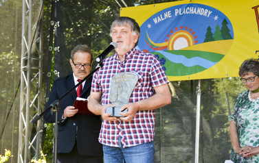 Mężczyzna w koszuli w kratę stoi przed mikrofonem i trzyma statuetkę Abasador Kociewia. Po Jego lewej stronie stoi drugi mężczyzna i coś czyta , a po prawej stoi kobieta.
