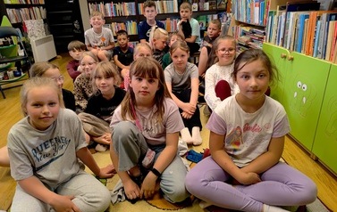 Dzieci siedzą na dywanie i słuchają czytanki.