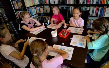 Dzieci siedzą przy stoliku i na białych kartkach wklejają obrazki dotyczące powstawania książki.