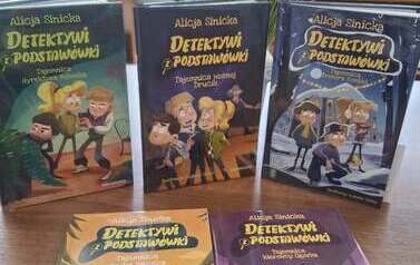 Na stole jest wyłożona nowa seria książek dla młodzieży " Detektywi z podstaw&oacute;wki"
