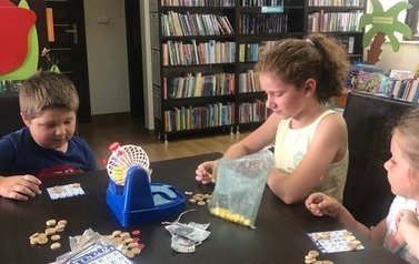 Dwie dziewczynki i chłopiec grają w bibliotece przy stolku w Bingo