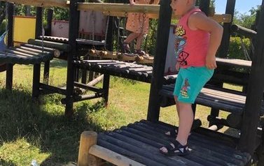 Chłopiec i dziewczynka chodzą po drewnianym mostku na placu zabaw przy biblliotece w Pinczynie