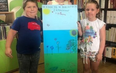 Dwie dziewczynki i chłopiec stoją pokazująć wsp&oacute;lnie namalowany plakat wakacyjny