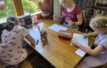 Trzy dziewczynki przy stole zaczynają coś malować na białych kartkach.