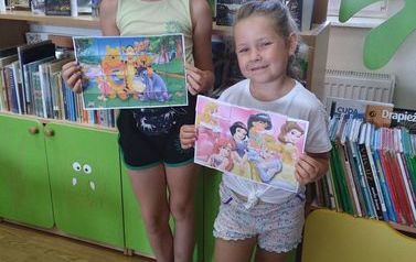 Dwie dziewczynki pokazują przyklejone na swoich kartkach puzzle z wizerunkiem Księżniczek i Kubusia Puchatka 