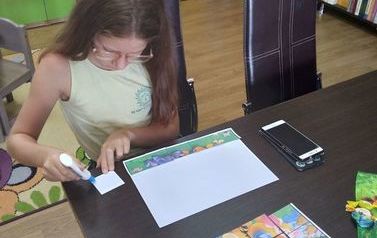 Dziewczynka przykleja na kartkę ułożone przez siebie puzzle z papieru z wizerunkiem Kubusia Puchatka.