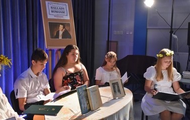 Trzy dziewczyny i chłopak przy stoliku na scenie trzymaja teksty do czytania. Na stoliku są postawione książki A. Mickiewicza