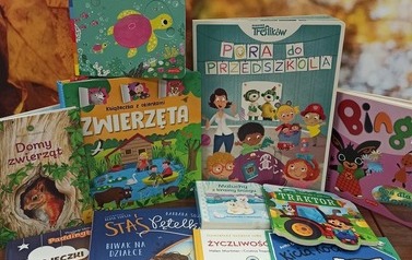 Nowe książki bajki ułożone na stoliku z widocznymi tytułami. W tle pejzaż z liśćmi.