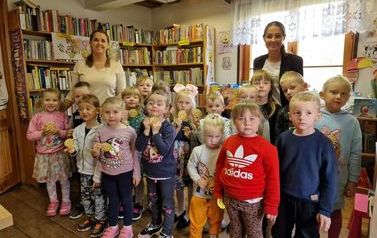 Zdjęcie grupowe dzieci z Panią Wychowawczynią i Pania bibliotekarką w bibliotece przy oknie.