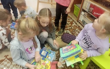 Dzieci siedzą na dywanie i przeglądają poduszkowe książeczki.