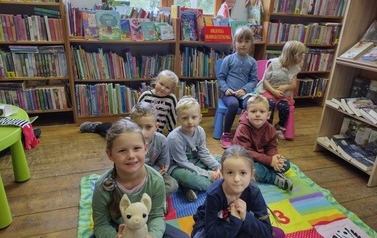 Dzieci siedzą na kocyku i patrzą w kierunku osoby robiącej zdjęcie.