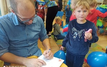 Chłopiec stoi przed bajkopisarzem, kt&oacute;ry podpisuje swoją książkę zakupioną przez dziecko.