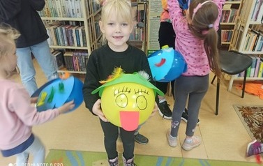 Dziewczynka pokazuje zwierzątko zrobione z balonika. W tle widać inne dzieci