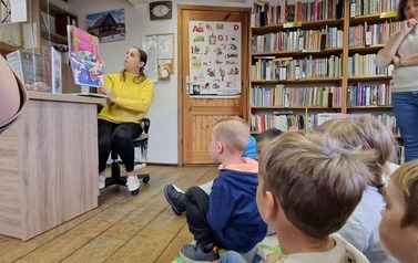 Dzieci siedzą na podłodze na kocyku, a Pani bibliotekarka czyta im bajkę