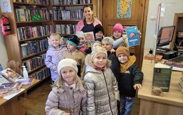 Dzieci stoją przed drzwiami przygotowane do wyjścia. Jedna dziewczynka pokazuje wyżej dyplom " Małego Czytelnika".