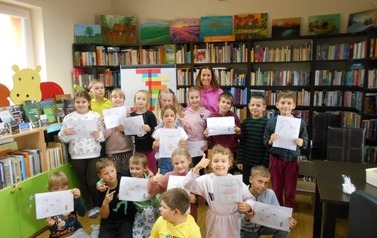 Zdjęcie grupowe na kt&oacute;rym jest nauczycielka i dzieci trzymające w rękach zrobione karty pracy.