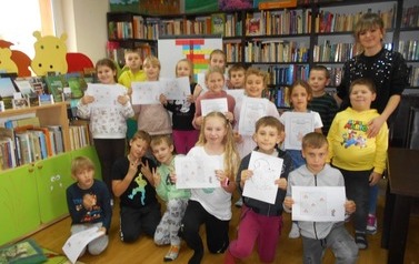 Zdjęcie grupowe na kt&oacute;rym jest bibliotekarka i dzieci trzymające w rękach zrobione karty pracy.