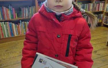 Dziewczynka w czerwonej kurtce stoi ze swoją wyprawką czytelniczą w bibliotece w Borzechowie