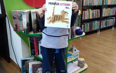 Chłopiec o blond włosach stoi w bibliotece w Pinczynie z nową książką.