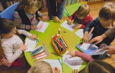 Dzieci siedzą przy okrągłym zielonym stoliku i robią pracę plastyczną.